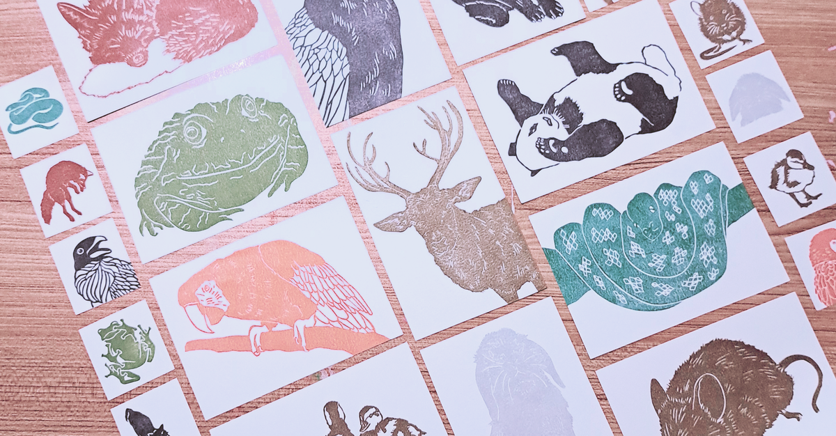 Staged photo of many animal themed lino prints on a wooden surface.