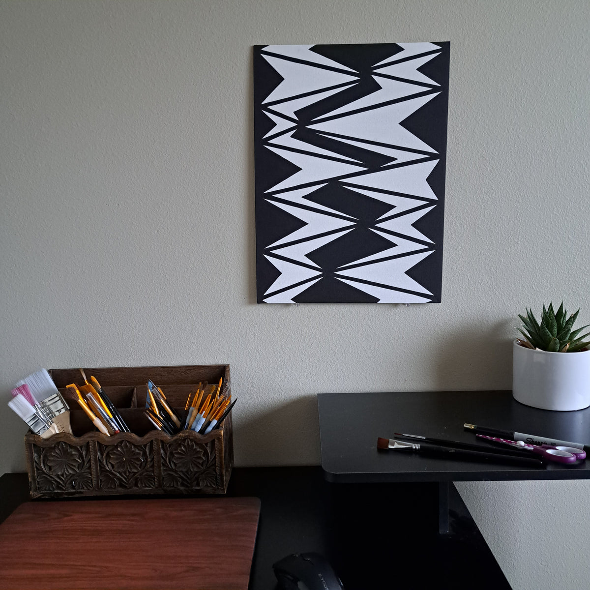 Staged photo of the "Oblique Darts" painting hung up on a a wall behind a desk