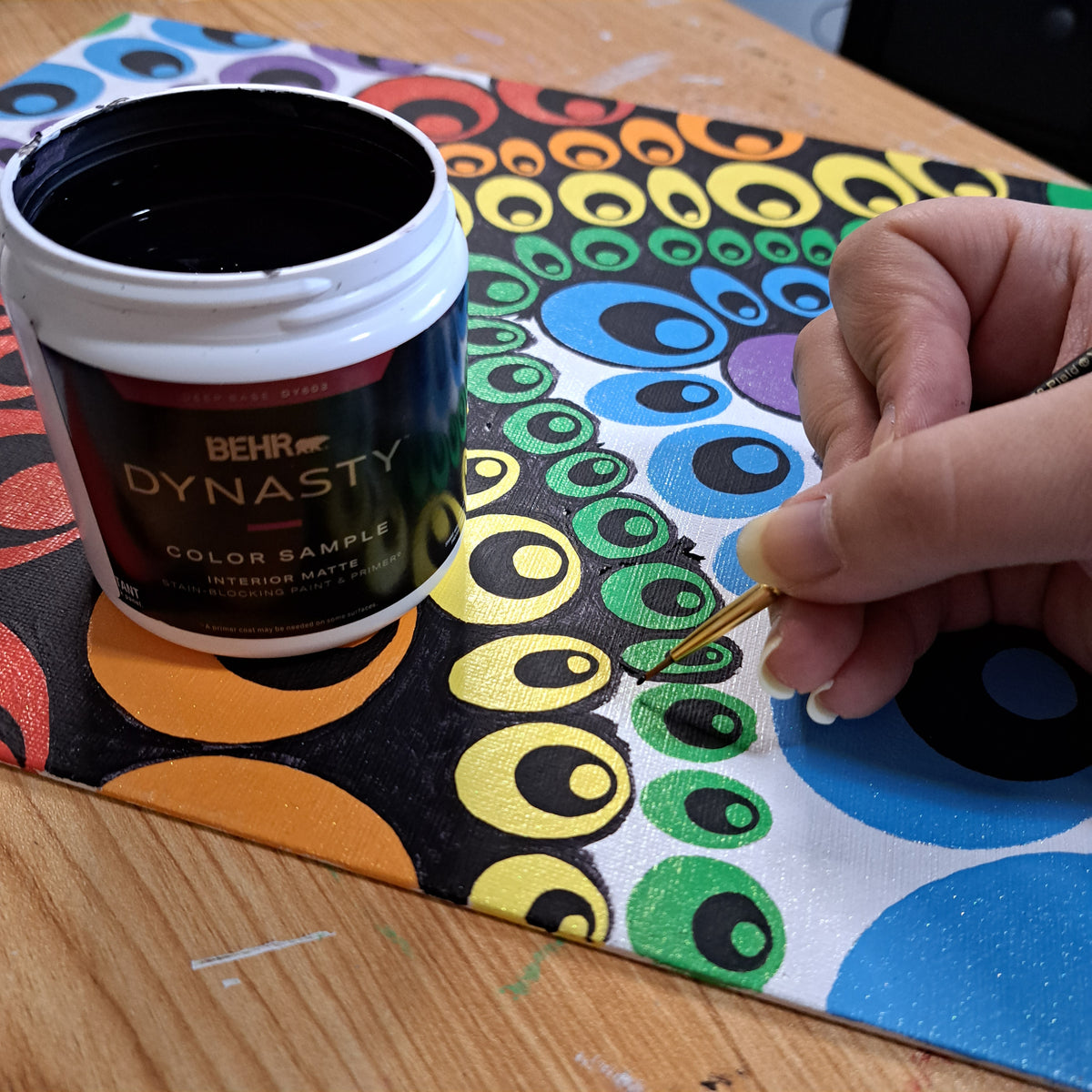 Photo of a hand holding a paintbrush over the "Rows of Teardrops" painting with a bottle of black house paint in the foreground